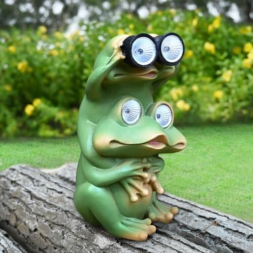 Two frog statues, one holding binoculars, on a log