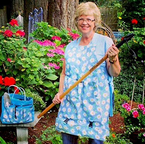 Smiling woman in a garden holding a tool, surrounded by flowers.