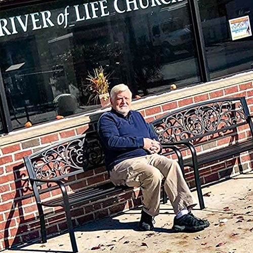 Man sitting on a bench outside a church with brick wall.