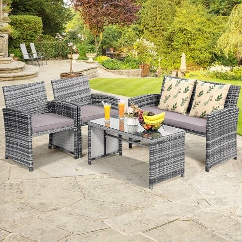 Gray wicker patio furniture set with cushions and glass-top table in a garden setting.