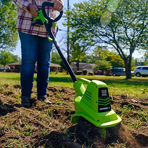 Person using a green electric tiller in a garden